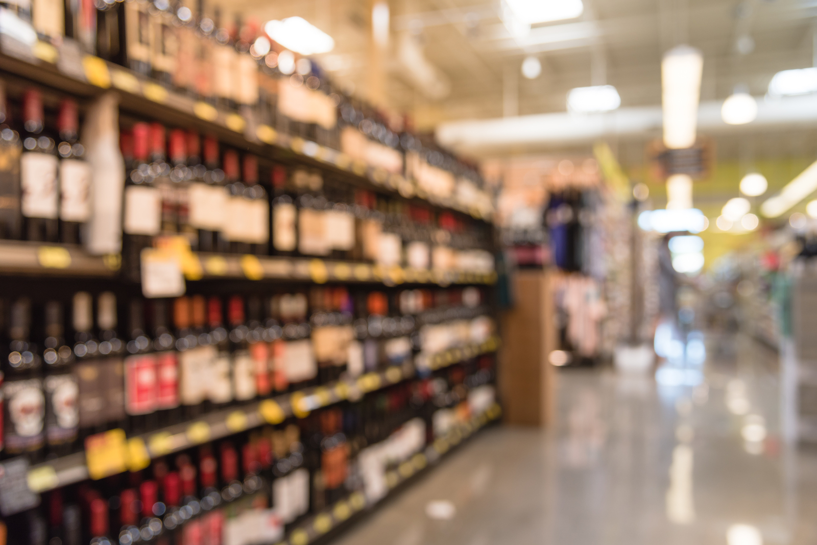 Blurred image of wine shelves with price tags on display in supermarket. Defocused  Rows of Wine Liquor bottles on the store shelf. Alcoholic beverage abstract background. Alcohol drink store concept